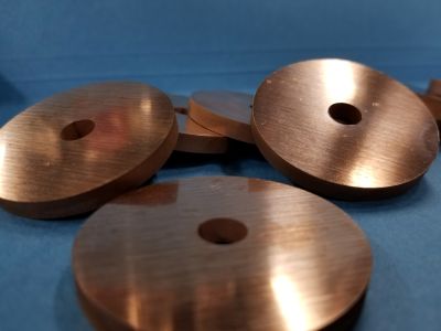 Specialty copper washers with center holes stacked on blue surface.