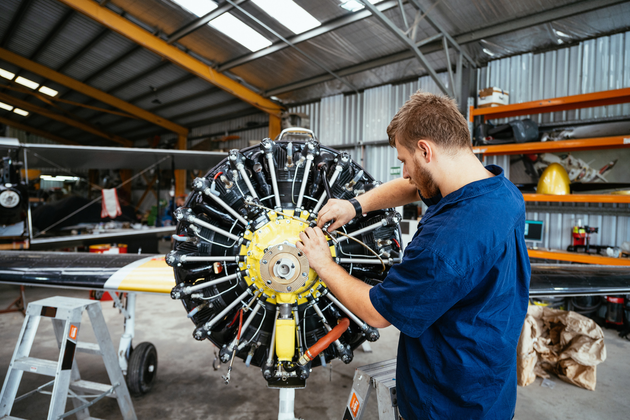 Aerospace mechanic working on a radial aircraft engine, tightening bolts and aircraft washer hardware in a hangar.
