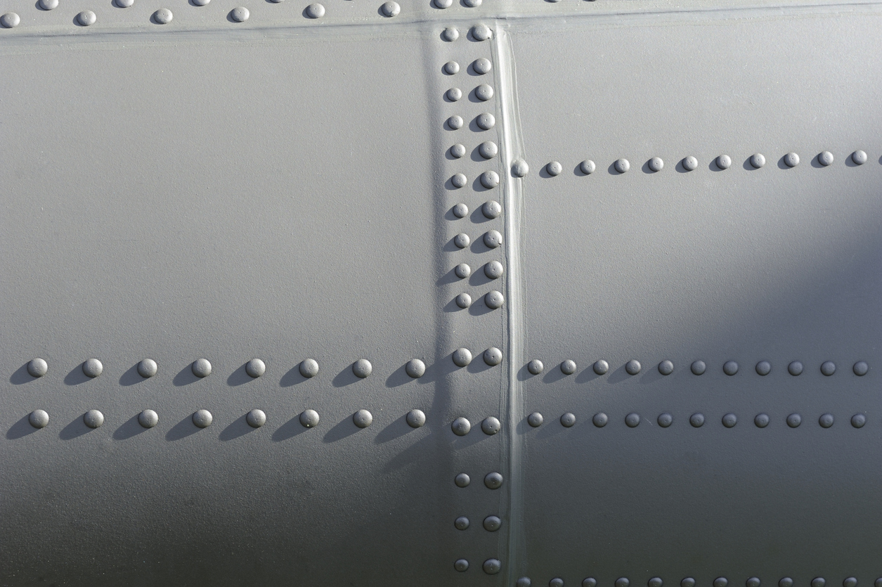 Close-up of gray metal aircraft panels joined by rows of military fasteners.
