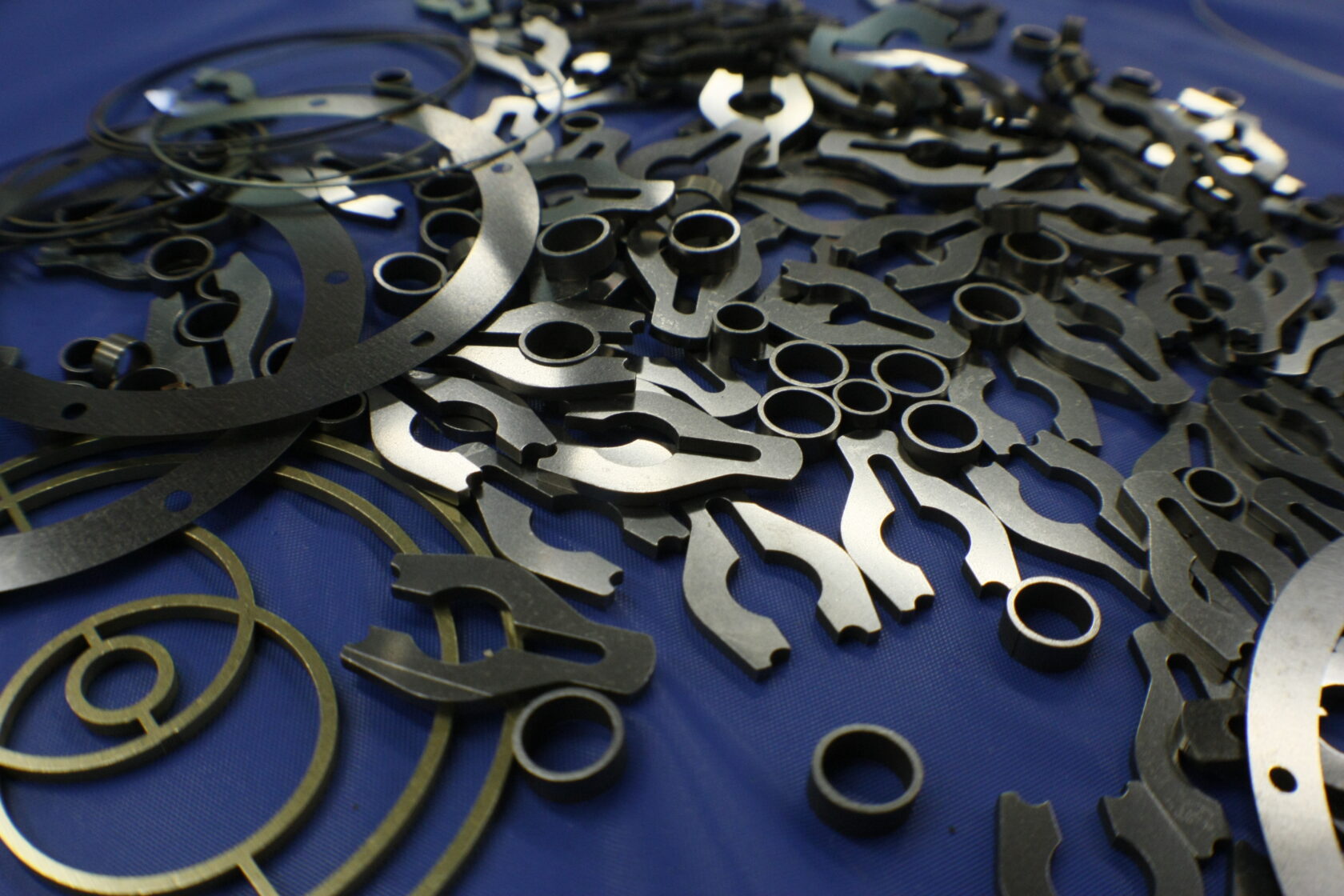 Assorted custom metal shims, from simple rings to multi-hole brackets, shown on a workbench.